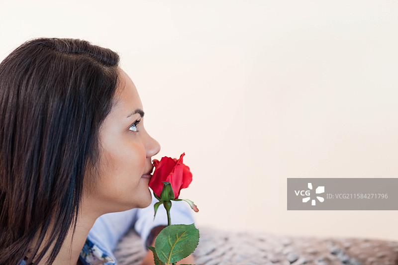 女人坐在有图案的沙发上闻红玫瑰，周围有空白空间图片素材