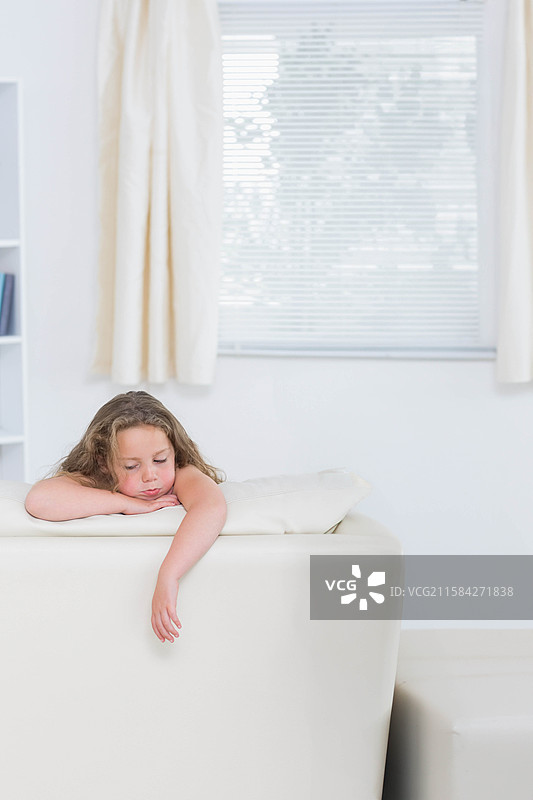 女孩子靠在明亮客厅的白色皮沙发上，窗帘微微拉开。图片素材