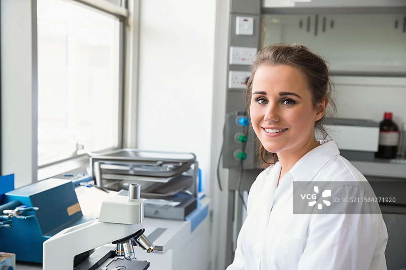 穿着实验室外套的女性科学家在工作台上用显微镜进行检查，旁边有托盘，留有空白空间图片素材