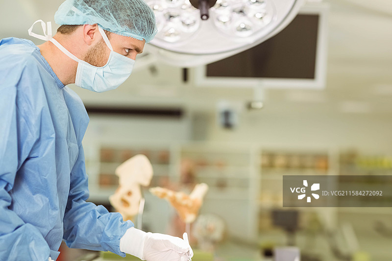 男性外科医生在手术室进行手术，手持手术刀，头顶有手术灯。图片素材