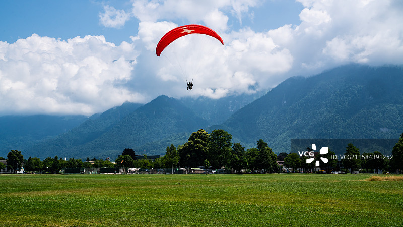 蓝天白云、草地和空中的红色滑翔伞。图片素材