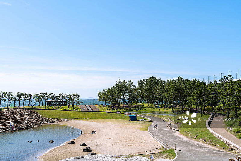 晴天灿烂光线里高视角下临海公园景色，波光粼粼的蓝色大海和岸边石凳图片素材