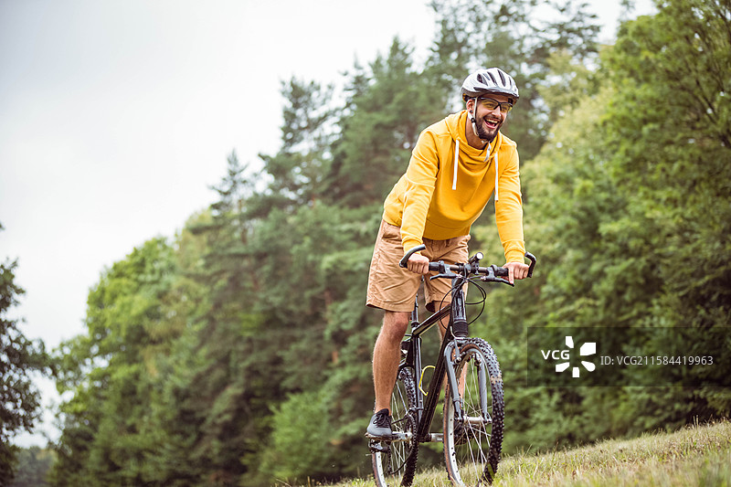 黑色山地自行车在森林中陡峭的草坡上攀爬，周围是高大的常绿树和落叶树。图片素材
