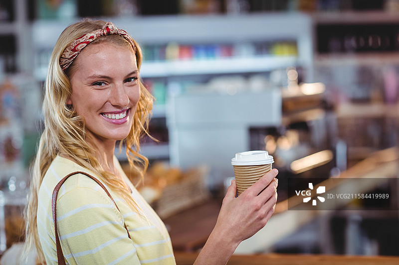 女人微笑着在咖啡馆的柜台前拿着带纹理的纸杯，背景有咖啡机，留有空白空间图片素材