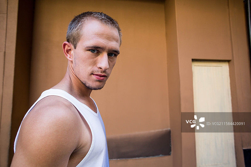 穿着白色背心的男子站在棕色灰泥墙旁的街道上，阴云密布，留有空白空间。图片素材