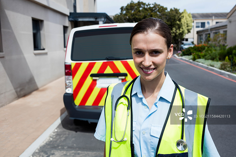 女性急救医务人员站在诊所外，身旁是带有斜纹的急救车辆，穿着背心和听诊器，留有空白空间。图片素材