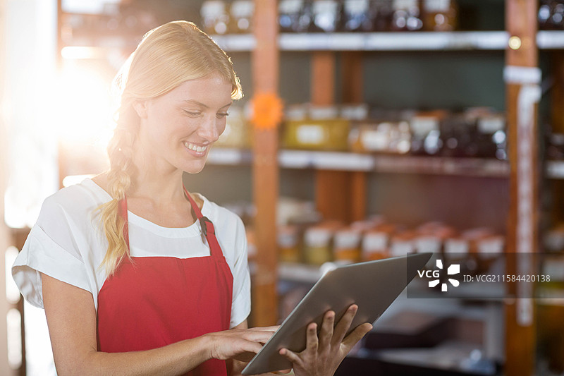 女店员站在精品店的木架旁，手持平板电脑检查玻璃罐。图片素材