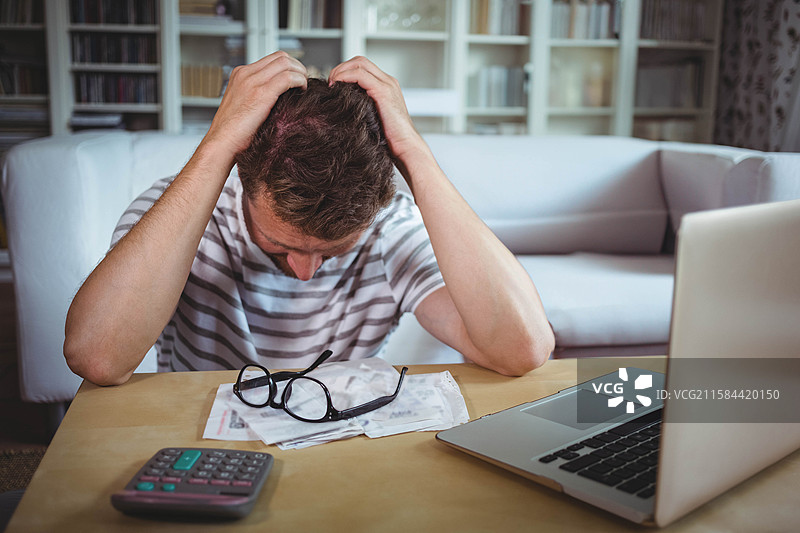 木桌上摆放着眼镜、散落的文件和计算器，旁边是一台打开的笔记本电脑，位于客厅中。图片素材