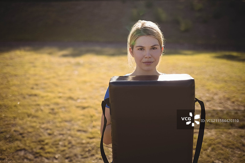 在阳光明媚的金色田野中，靠近阴凉灌木丛，胸前抱着训练垫，正值下午晚些时候。图片素材