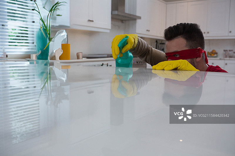 男子戴着黄色手套，用绿色海绵擦洗现代厨房的白色台面岛。图片素材