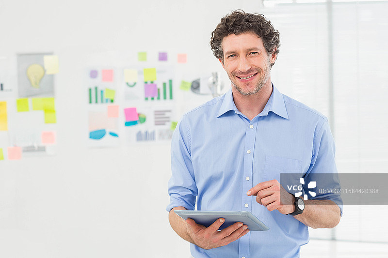 男子在办公室用手指轻触平板电脑屏幕，手腕上戴着手表，周围有便利贴和图表。图片素材