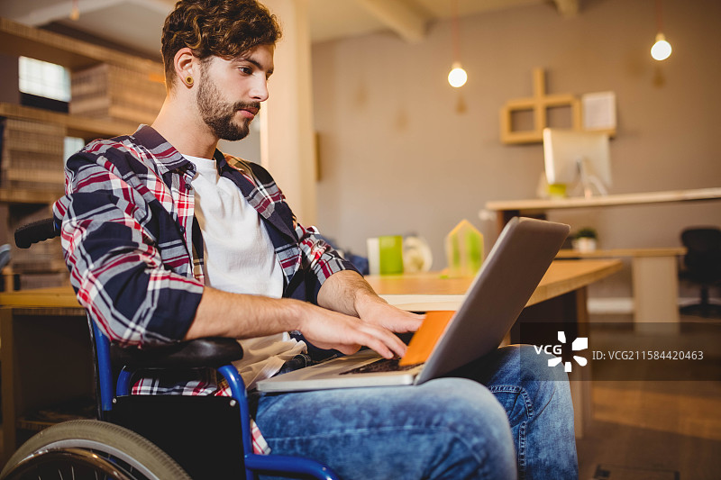 笔记本电脑放在轮椅上，旁边是木制桌子，悬挂的吊灯照亮了共享办公空间。图片素材