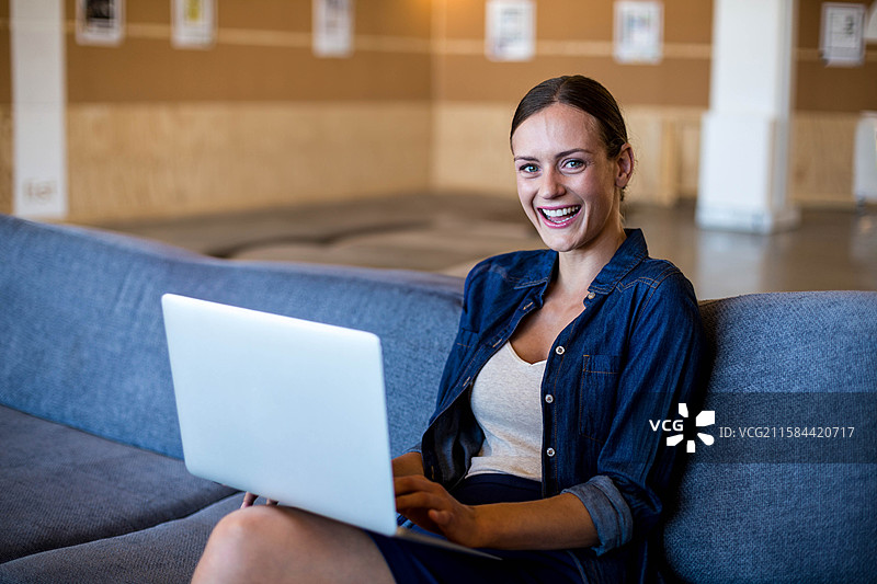 现代办公室休息区的深灰色沙发上放着一台笔记本电脑，背景是软木公告板。图片素材