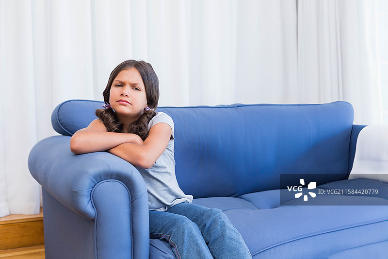 一个学龄女孩靠在客厅蓝色沙发的扶手上，白色窗帘，留白空间图片素材