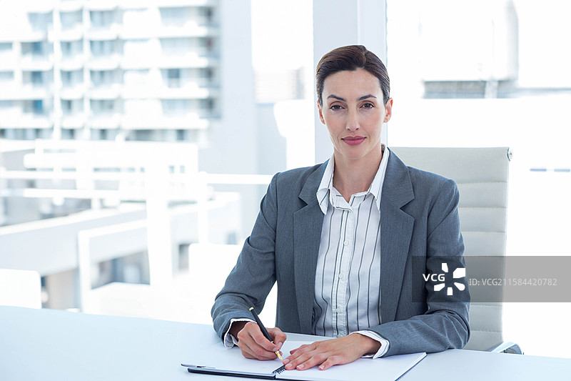 中年职业女性在阳台栏杆旁的桌子上用黑色钢笔在笔记本上写字图片素材