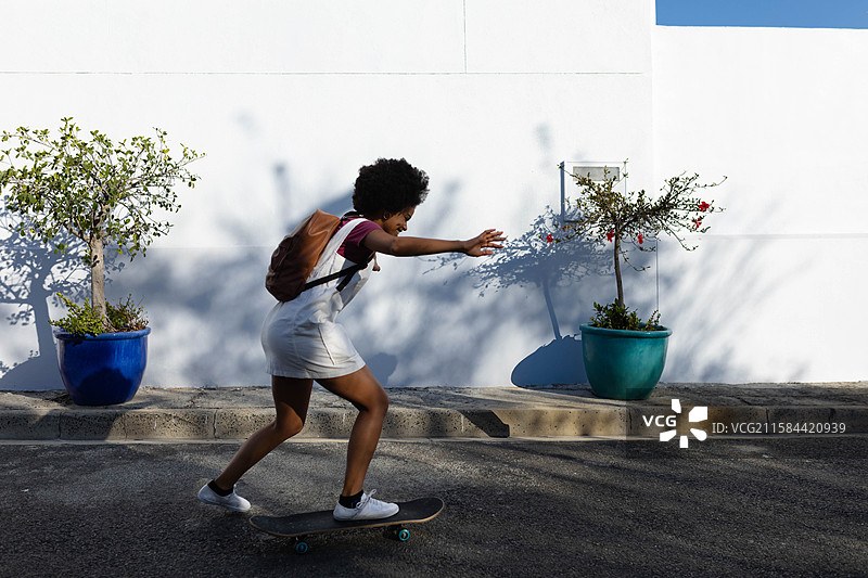 滑板运动员向前倾斜，平衡在靠近白色墙壁的街道上，周围有五彩缤纷的花盆。图片素材
