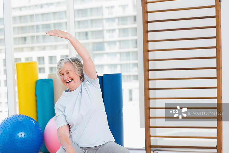 老年女性在健身工作室的泡沫垫上做侧弯拉伸，旁边有泡沫滚筒，留有空白空间。图片素材