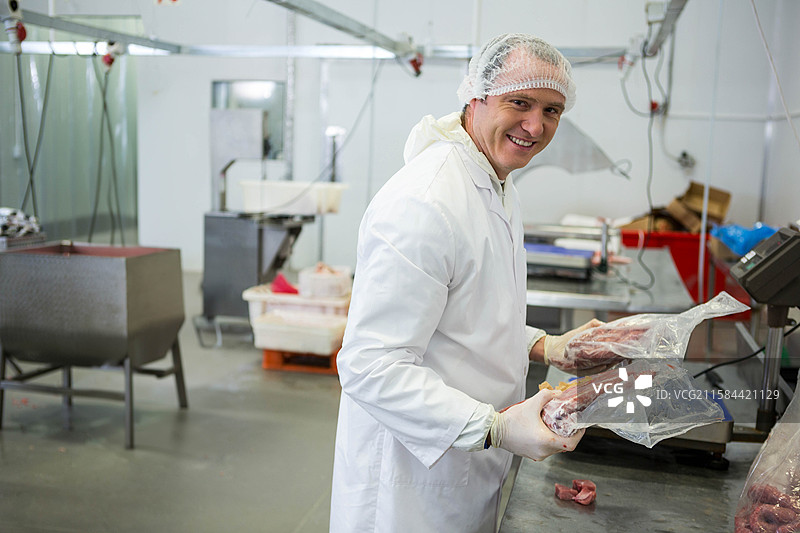 中年男子戴着发网在肉类加工厂的金属桌上处理肉块，留有空白空间图片素材
