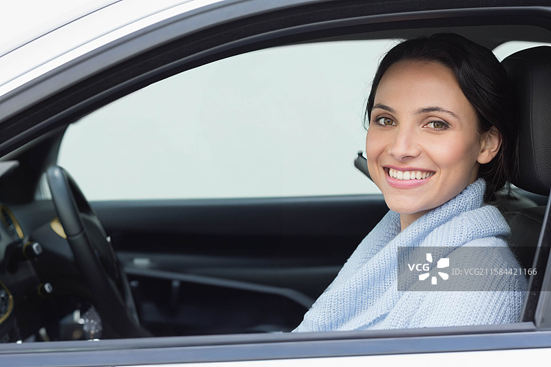 穿着浅蓝色毛衣的女性微笑着握住方向盘，坐在停着的车内，留有空白空间。图片素材