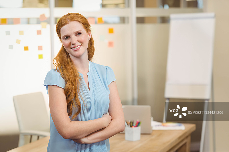 红发女性在办公室的桌子上交叉双臂，旁边有便利贴和翻转图表图片素材