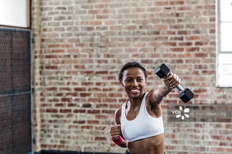 非裔美国女性在健身工作室用哑铃挥拳，手腕缠绕粉色护腕。图片素材