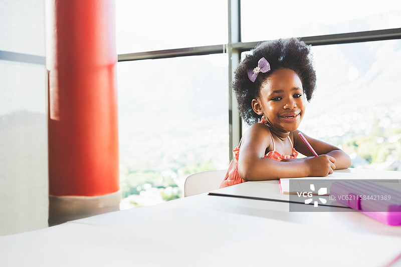 非裔美国女孩在窗边的桌子上用粉色铅笔盒写笔记本，留有空白空间图片素材