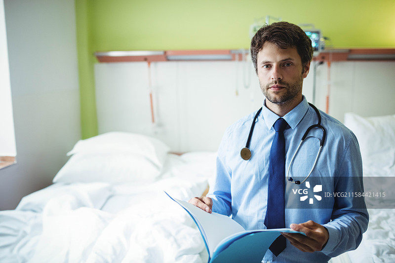 男医生站在病床旁边，使用听诊器查看病人档案，留有空白空间图片素材