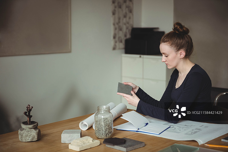 女性坐在设计工作室的桌子旁，检查瓷砖样品，桌上有一罐石头，留白空间图片素材