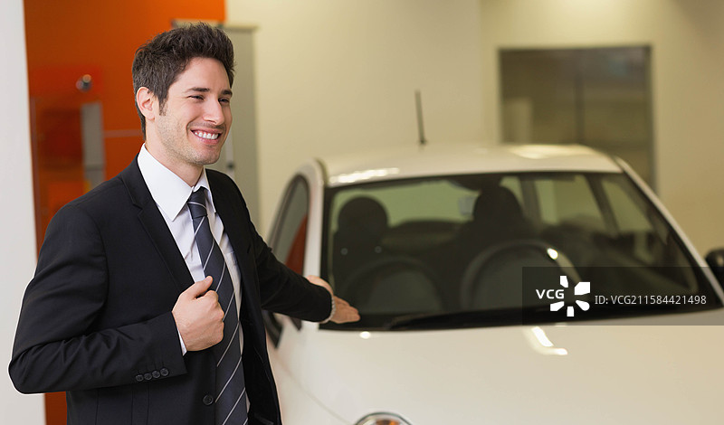 男性站在汽车展厅展示白色紧凑型车，留有空白空间图片素材