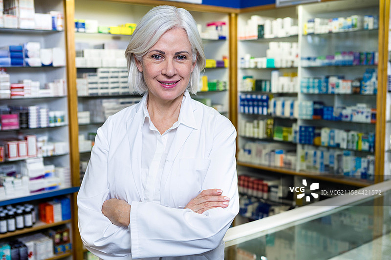 穿着实验室外套的资深药剂师在药房的玻璃柜台后整理药品盒子。图片素材
