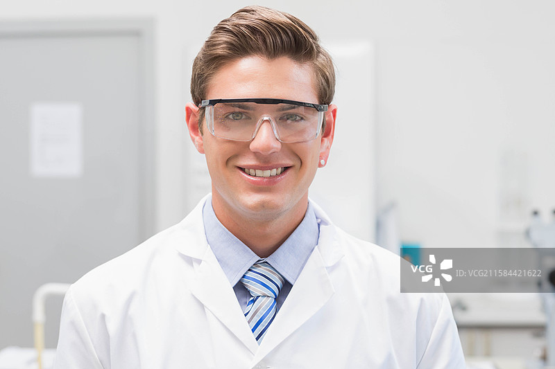 男性实验室研究员穿着白色实验室外套和安全护目镜，站在实验台前。图片素材