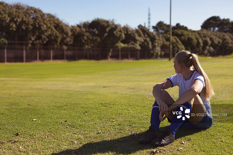 公园草地上坐着的足球运动员，穿着白色球衣、蓝色短裤和黑色足球鞋图片素材