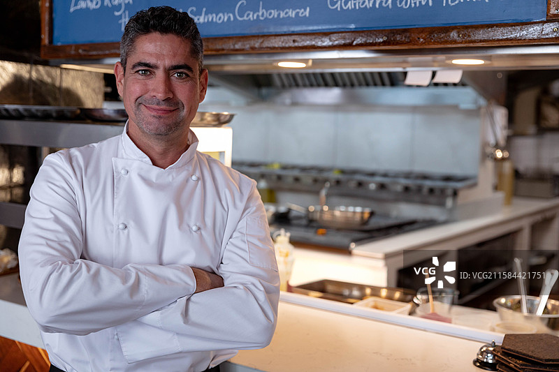 成熟男性厨师双臂交叉站在厨房服务台后，留有空白空间图片素材