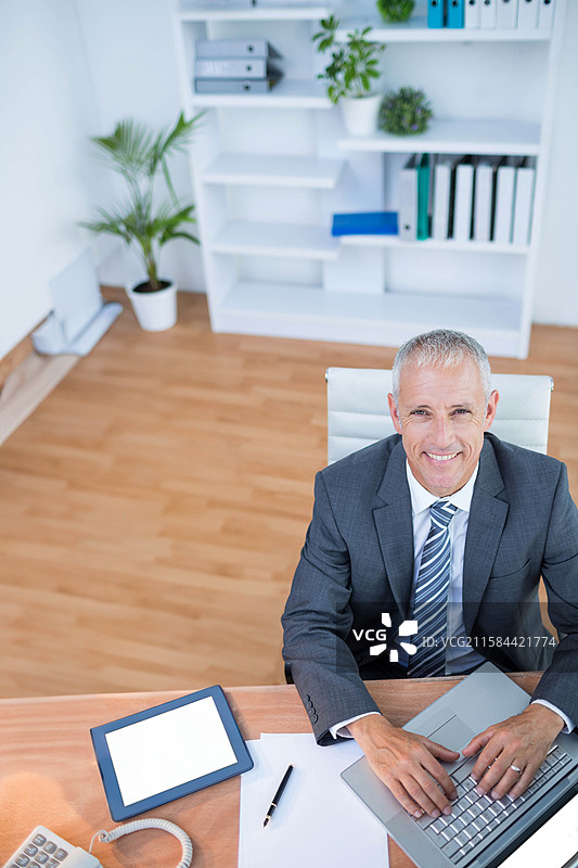 穿着商务服装的中年男子在办公室的桌子上使用笔记本电脑，留有空白空间图片素材