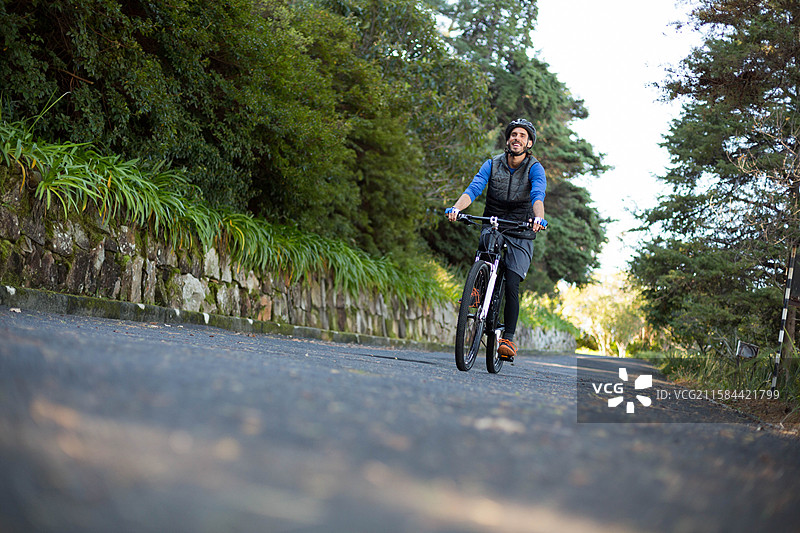 男性骑着自行车，佩戴着头盔和背包，沿着乡村道路骑行，旁边是石墙。图片素材
