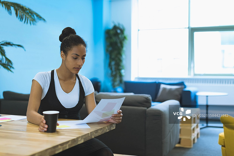 非裔美国女性在共享办公桌上手持打印文件，喝着咖啡，留有空白空间图片素材