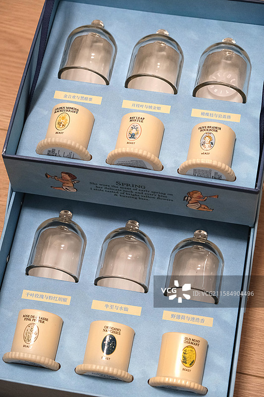 标题：六款香型香薰蜡烛礼盒特写 金合欢与黑醋栗/月桂叶与桃金娘等 玻璃罩+浅蓝内衬 木质桌面静物图片素材