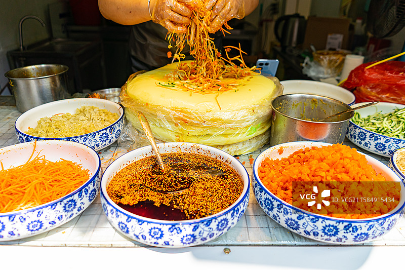 中国餐饮行业饮食经典中国食品拍摄主题，老板正制作手工卷凉皮超薄越南米皮卷和一堆配菜，户外白昼人物图像图片素材