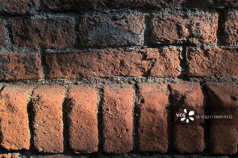 夕阳树影斑驳洒在一片红砖墙上，岁月已经侵蚀了这片老墙，红砖表面表明已经完全被风化掉了图片素材