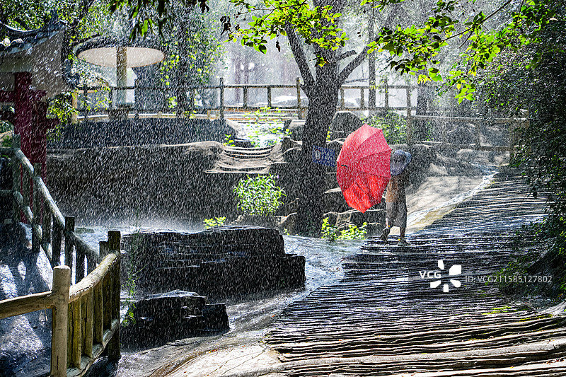 山东济南金象山乐园彩虹谷，一个小男孩打着一把红伞，在雨中步行图片素材