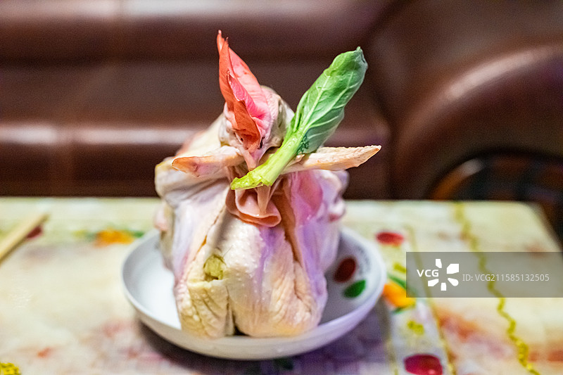 中国传统农业文化祭祀拍摄主题，桌子上盘子里的盘起来的公鸡和绿色油菜配菜，室内无人图像摄影图片素材