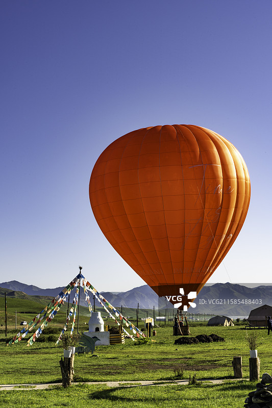 清晨的甘加草原，一只鲜艳的红色热气球正在营地旁缓缓升空，与远山、帐篷和经幡交相辉映图片素材