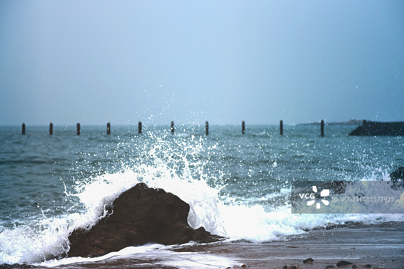 海浪拍打岩石，远处木桩点缀图片素材