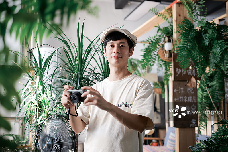 在绿植主题咖啡馆拿着相机的男性图片素材