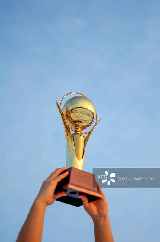 双手高举奖杯，蓝天背景图片素材