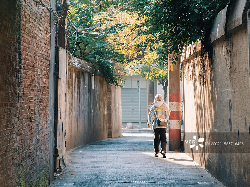 一个女孩走在阳光照进红砖巷子图片素材