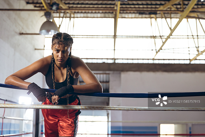 非裔美国女性拳击手穿着运动胸罩，在拳击馆的擂台上靠在绳子上训练。图片素材