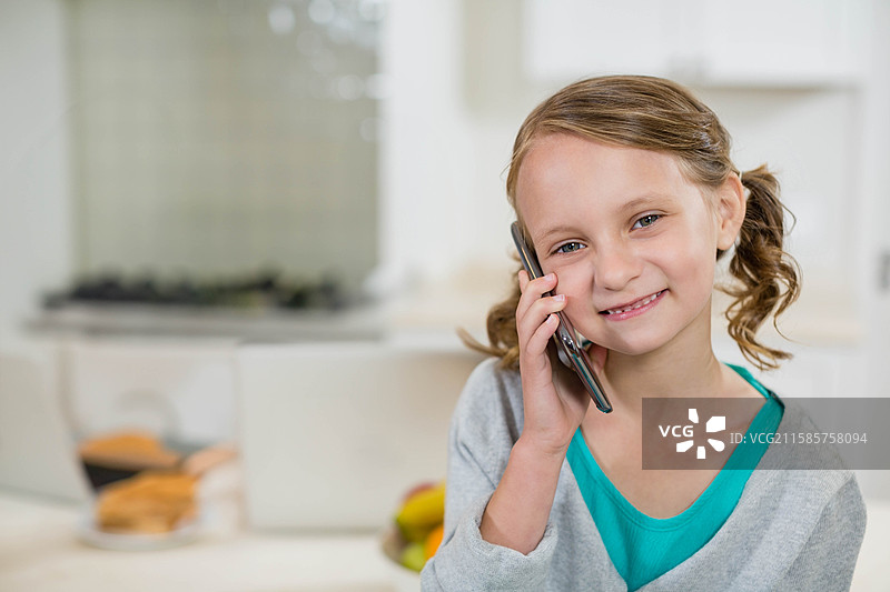 女孩在厨房里靠近水果碗和面包，手持智能手机靠在耳边，留有空白空间图片素材