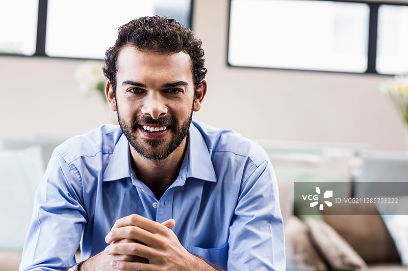 穿着衬衫的商人在沙发靠垫的休息室里微笑着向前倾身。图片素材