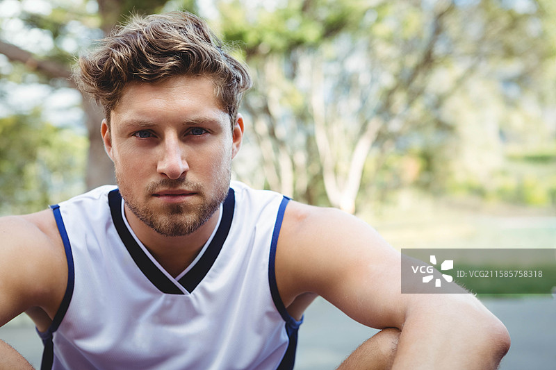 男性运动员蹲在铺砌的公园球场上，穿着无袖的白色和海军蓝运动衫。图片素材